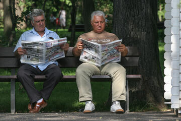 Two men are reading a newspaper on a bench in Bucharest
